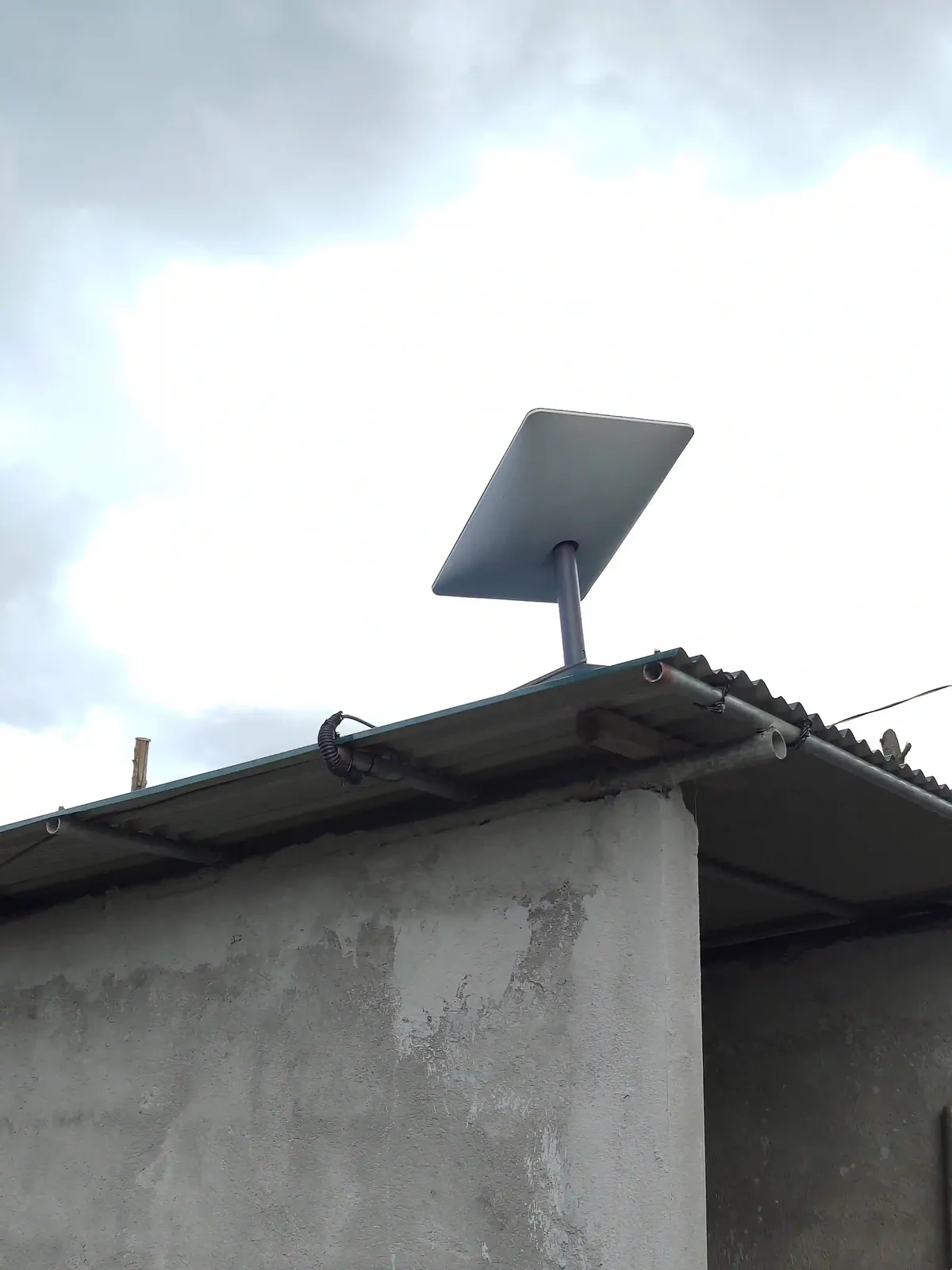 A Starlink dish mounted on a pole at the edge of a shed roof against the sky.