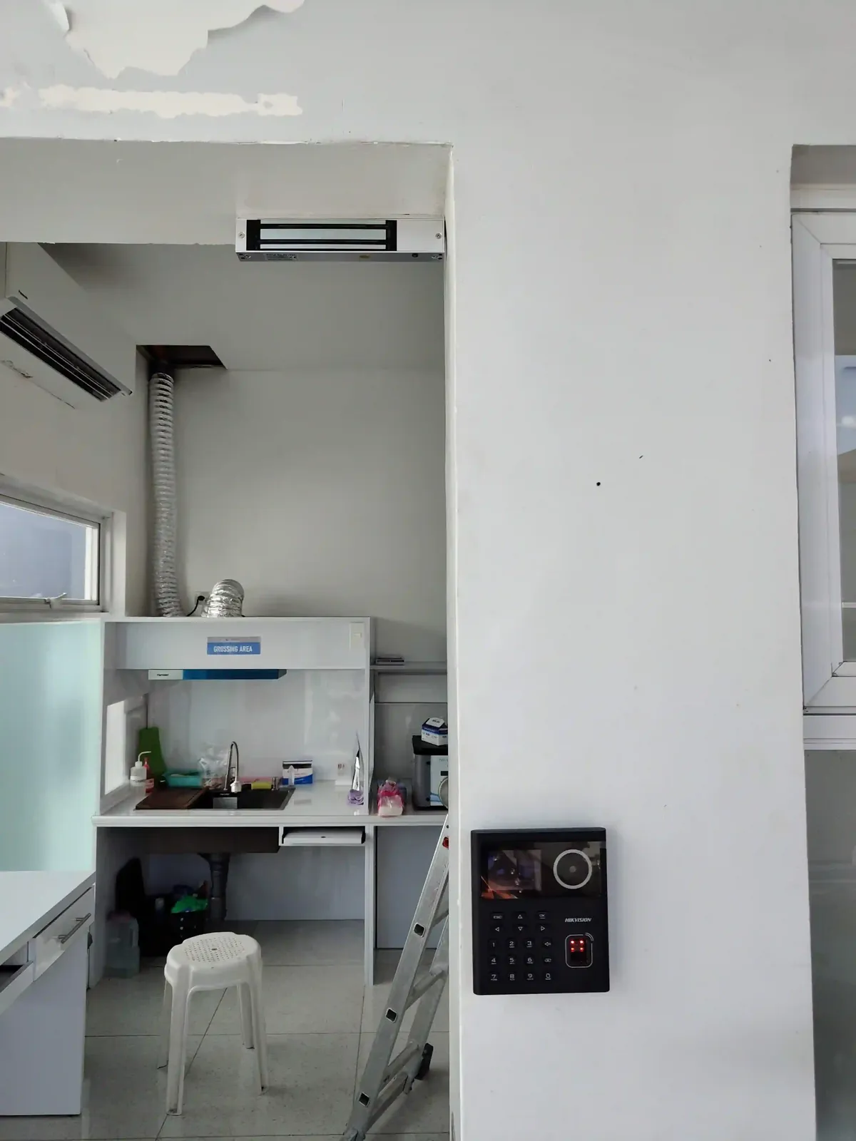 A Hikvision keypad-and-fingerprint access terminal mounted by a door.