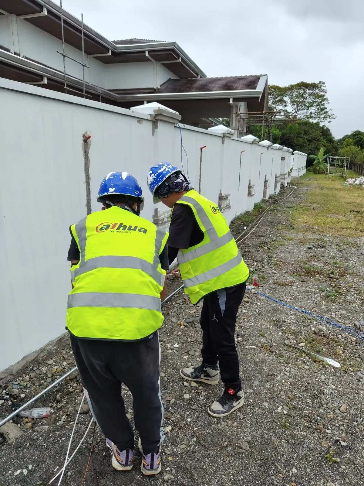 Two workers in hard hats and hi-vis vests working at a perimeter wall.